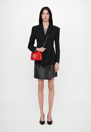 Black fitted blazer with shoulder pads, paired with a black leather skirt. Holding a glossy red handbag with a gold logo. Black heels.
