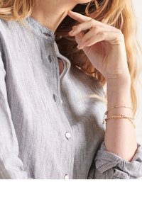 Camicia a righe in grigio chiaro e bianco, con colletto a serafino e maniche arrotolate. Mano adornata con bracciali d'oro a strati.