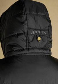 Černá péřová bunda s prošívanou kapucí a viditelnou logovkou. Materiál vypadá hladce s lesklým povrchem. Doplňky ve zlaté barvě.