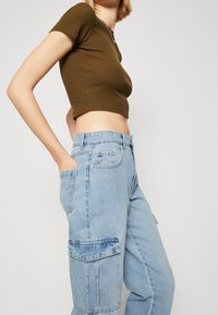 Top corto de canalé en verde oliva combinado con pantalones cargo de mezclilla azul claro, que presentan bolsillos laterales y un ajuste relajado. Tela texturizada visible.