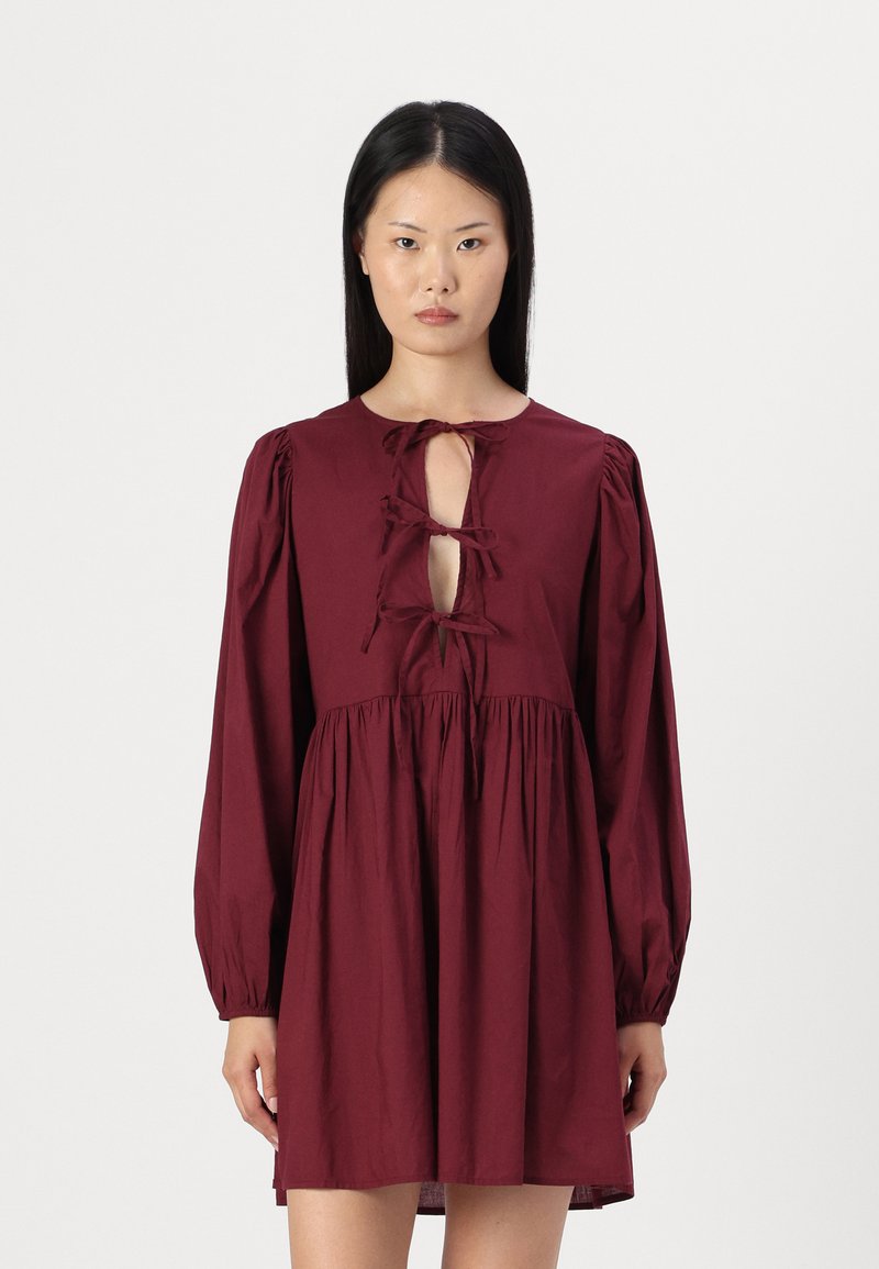 Vestido burgundy com mangas largas bufantes, decote redondo e detalhe em forma de buraco na frente, com laços e cintura franzida.
