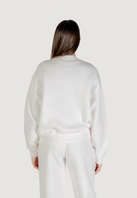 Biały sweatshirt z mieszanki bawełny z okrągłym dekoltem, opadającymi ramionami i prążkowanymi mankietami. Charakteryzuje się luźnym krojem i miękką fakturą.