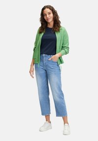 Zielony sweter z zamkiem, granatowa bluzka, jasnoniebieskie jeansy 3/4 i białe sneakersy. Sweter posiada troczki u dołu oraz teksturowany materiał.