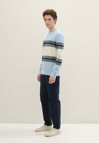 Hellblau gestreifter Pullover mit grauen und schwarzen horizontalen Streifen, kombiniert mit marineblauen Hosen und beigen Sneakers. Weiches Material, lässige Passform.