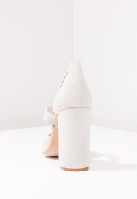 Suedesandal i ljusgrått med tjock klack. Har en bakrem och öppen tå-design. Slät textur och minimala detaljer.