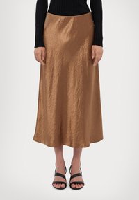 Brun sateng lang maxi skjørt med en glatt tekstur, som har en lett krøllete overflate, sitter i livet, kombinert med svarte høyhælte sandaler.