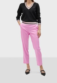 Svart v-halsad tröja med randiga manschetter och en liten logga, i kombination med ljusrosa taperade byxor och svarta spetsiga ballerinas.