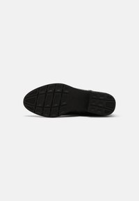 Suela de zapato negra que presenta un material de goma con un patrón texturizado y un diseño de banda de rodadura estructurado para ofrecer agarre y durabilidad.