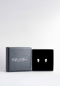 Sølv kranium stud øreringe præsenteret i en sort velourforet boks med en tekstureret sølvoverflade og "Sofia Milani Jewels" branding.