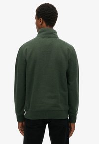 Groene fleece trui met een hoge kraag, ribgebreide manchetten en zoom. Gladde textuur, eenvoudig ontwerp en een klein naaddetail op de rug.