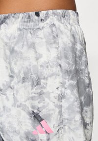 Gros plan de shorts de sport tie-dye gris et blanc avec un logo rose Adidas près de la poche et une taille élastique à la taille d'une personne.