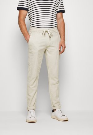 Bežové lněné kalhoty s elastickým pasem, slim fit a ohrnovacími manžetami. Spárovány s černobílým proužkovaným tričkem s krátkým rukávem a bílými teniskami.