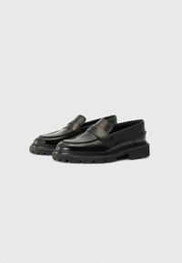 Mocassins en cuir noir avec une semelle basse et épaisse, un bout arrondi et une finition lisse. Équipés d'une sangle décorative sur le devant.
