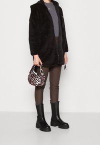 Chaqueta de cremallera negra y peluda, blusa gris de canalé, pantalones marrones ajustados, botas negras gruesas y un pequeño bolso de leopardo.