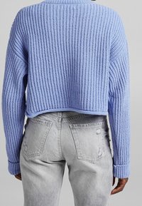 Personne portant un pull texturé bleu clair et un jean taille haute gris clair avec des poches arrière et une légère déchirure.