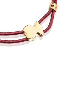 Charm en tono dorado en una pulsera de cordón de satén burdeos y rosa. Presenta una forma abstracta lisa y un detalle metálico.