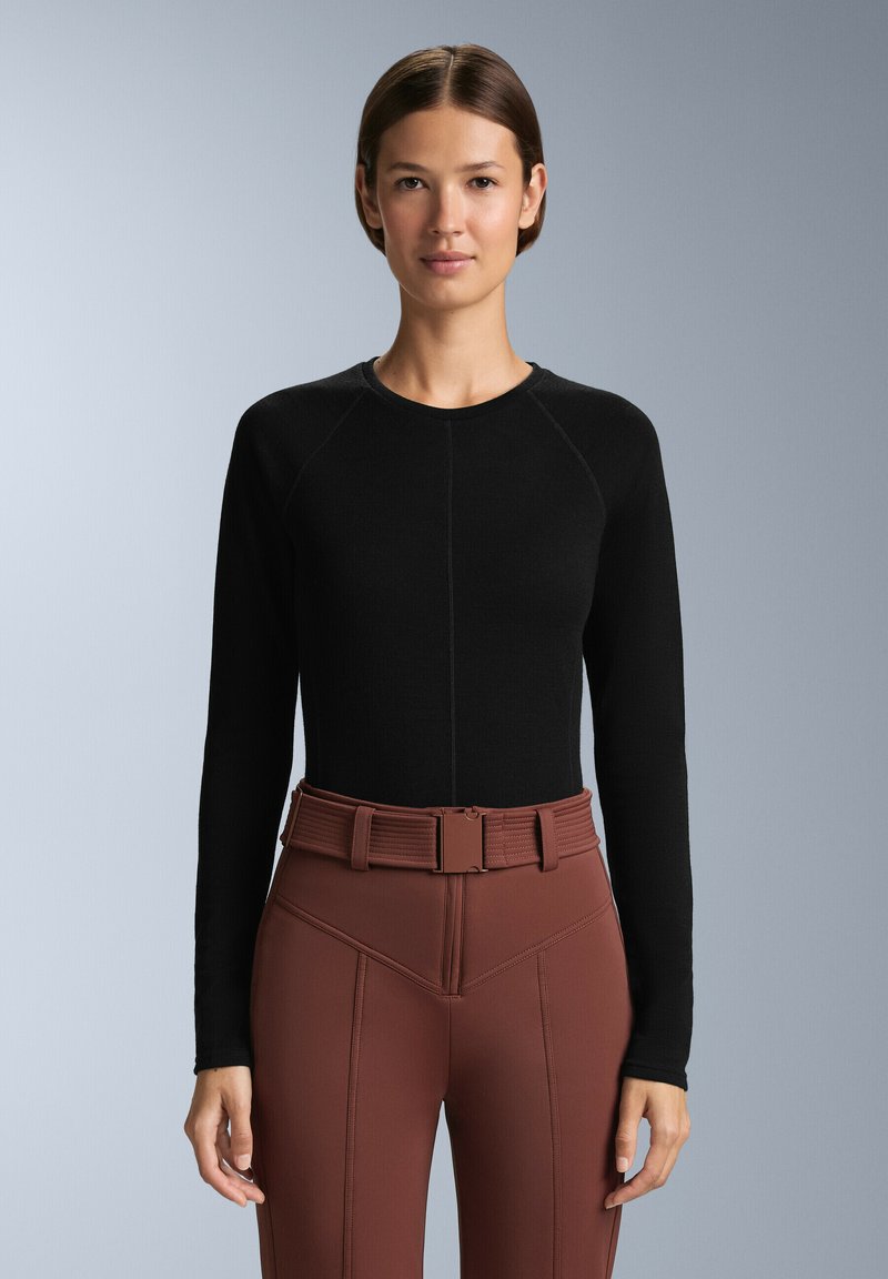 Svart långärmad topp med rund halsringning och raglanärmar. Matchad med högmidjade, bruna tajta byxor med ett strukturerat bälte.