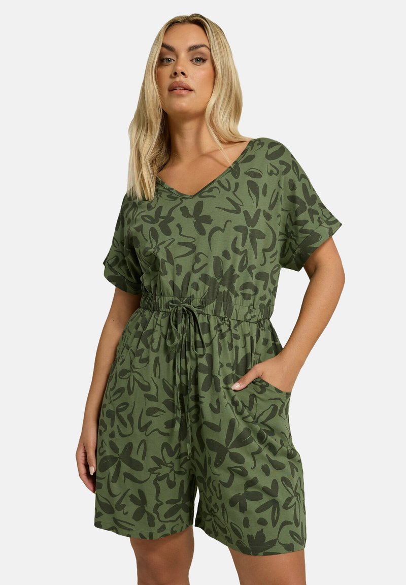 Combinaison courte verte avec décolleté en V, manches courtes, taille élastique et motif floral foncé sur l'ensemble. Comprend des poches latérales.