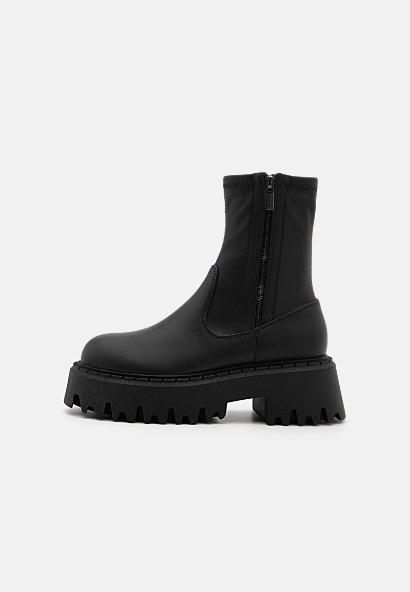 Bottes noires à la cheville en matériau synthétique lisse. Dotées d'une semelle épaisse et crantée ainsi que d'une fermeture éclair sur le côté pour un enfilage facile.