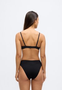 Μαύρο μπικίνι με ρυθμιζόμενους λεπτούς ιμάντες και κούμπωμα. Σλιπ ψηλόμεσο με υφασμάτινη υφή. Απλός σχεδιασμός μονόχρωμος.