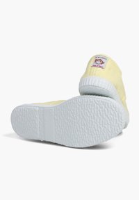 Żółte płócienne buty z teksturowaną białą gumową podeszwą, z małą łatką logo z tyłu. Buty wykazują minimalne oznaki użytkowania.
