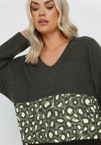 Przesadny sweter z dekoltem w serek w ciemnozielonym kolorze, z panelem w jasnym kremie i zieleni w wzór lamparta. Miękka tekstura i luźny krój.