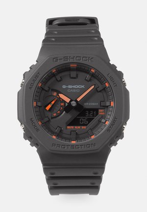 G-Shock laikrodis su matinio juodo plastiko dirželiu, oranžinėmis detalėmis, skaitmeniniu ekranu ir analoginiais rodyklėmis. Atsparus vandeniui iki 20 barų.