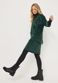 Gröna kordtäckta skjortan och kjolen i set, i kombination med svarta anklarboots. Skjortan har en krage och knapprad; bootsen har texturerade sulor.