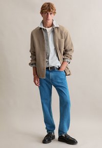 Bruin textuur overhemd over een gestreept overhemd met knopen, gecombineerd met een blauwe spijkerbroek en zwarte loafers. Ontworpen met een ontspannen pasvorm en een casual stijl.