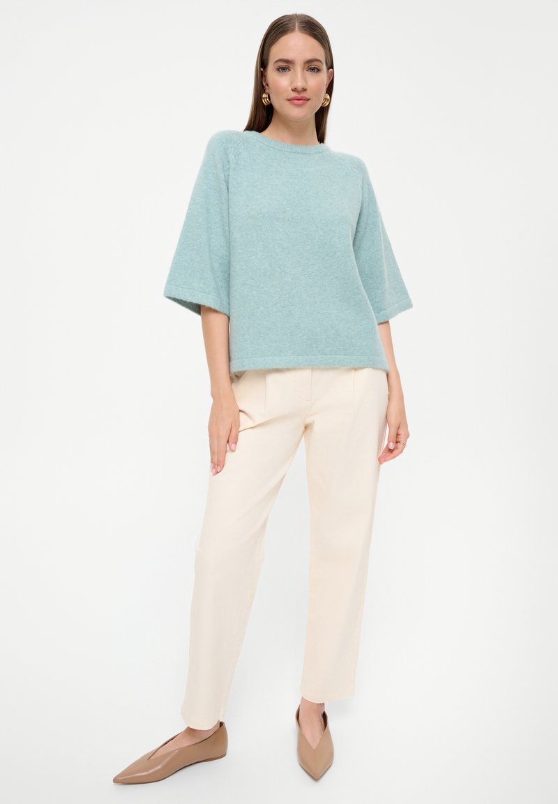 Lichtblauwe, korte mouwen, losgebreide trui gecombineerd met beige, taps toelopende broek en puntige, lichtbruine flats. Eenvoudig en textuurvol ontwerp.