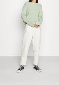 Vaaleanvihreä neulottu lyhyt villapaita, jossa on väljä istuvuus, yhdistetty norsunluunvärisiin leveälahkeisiin housuihin ja mustiin korkeavartisiin tennareihin.