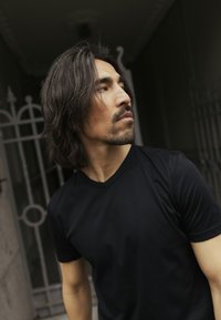 Juodas trumpomis rankovėmis V formos kaklo marškinėlis iš lygaus audinio, puikiai prigludęs ir su subtiliu logotipo akcentu ant rankovės.