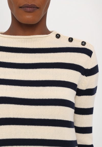 Maglione a righe con colori crema e blu navy, texture a maglia e tre bottoni neri sulla spalla sinistra.