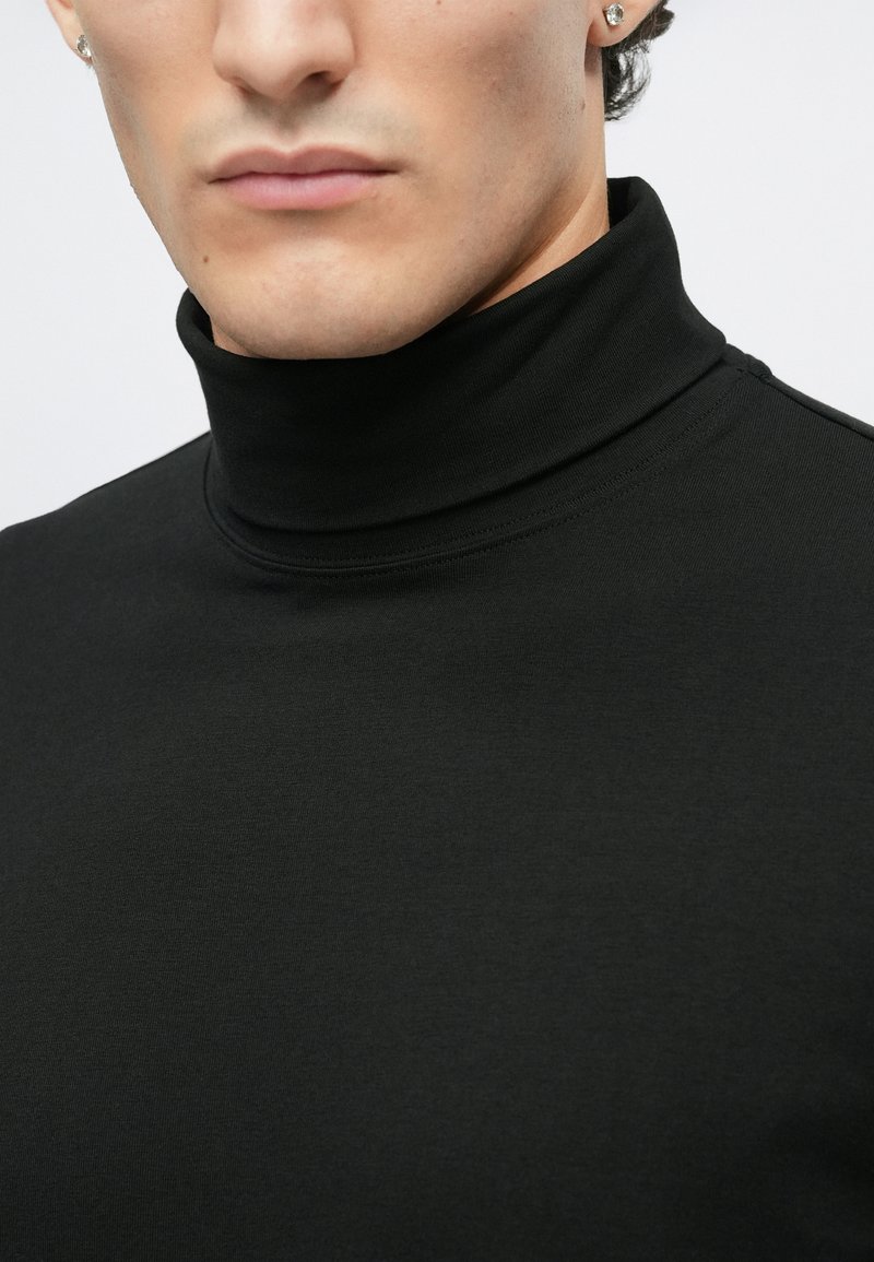Sort turtleneck top lavet af glat, strækbart stof. Har et tætsiddende design med en høj krave og minimale syninger.