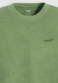 Zaļš kokvilnas kreklu ar garām piedurknēm, ar izsmalcinātu tonālu "Levi's" logo, gludu struktūru un vintage stila piegriezumu.
