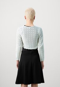 Svetle modrý pletený cardigan s krajkovým vzorem, dlouhými rukávy a zakulaceným výstřihem, spárovaný s černou sukni ve tvaru A.