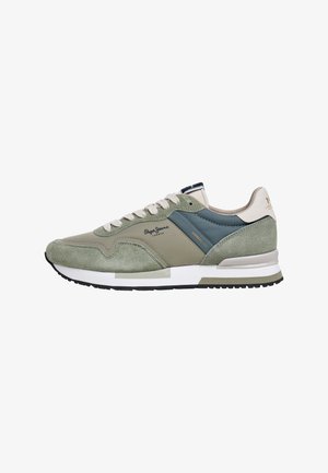 Grüne Wildledersneakers mit einem marineblauen Stoffakzent, beigen Schnürsenkeln und einer weißen Sohle. Auf der Seite befindet sich ein gut erkennbares Markenlogo.