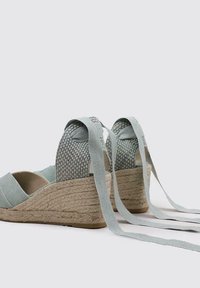 Zapatos de cuña de lona azul claro con suelas de yute trenzado, que presentan un acabado texturizado en la parte trasera y largas cintas de tela para asegurar alrededor del tobillo.