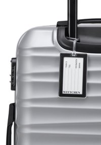 Silver hardshell suitcase with a textured surface, retractable black handle, and a removable identification tag attached to the side.