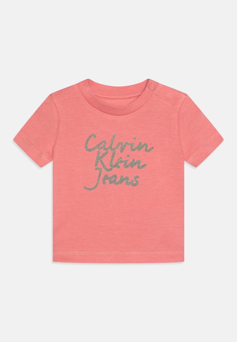 Coral cotton T-shirt with short sleeves and a round neckline. Features silver glitter text "Calvin Klein Jeans" across the front.