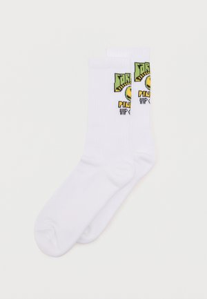 Calzini bianchi da ginnastica con grafica verde e gialla sul polsino, con testo stilizzato e design di una faccina sorridente.