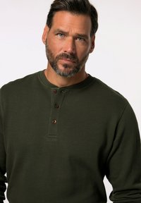 Olijfgroene langlopende henley shirt met een geribbelde textuur, voorzien van drie bruine knopen bij de kraag en een ronde halslijn.