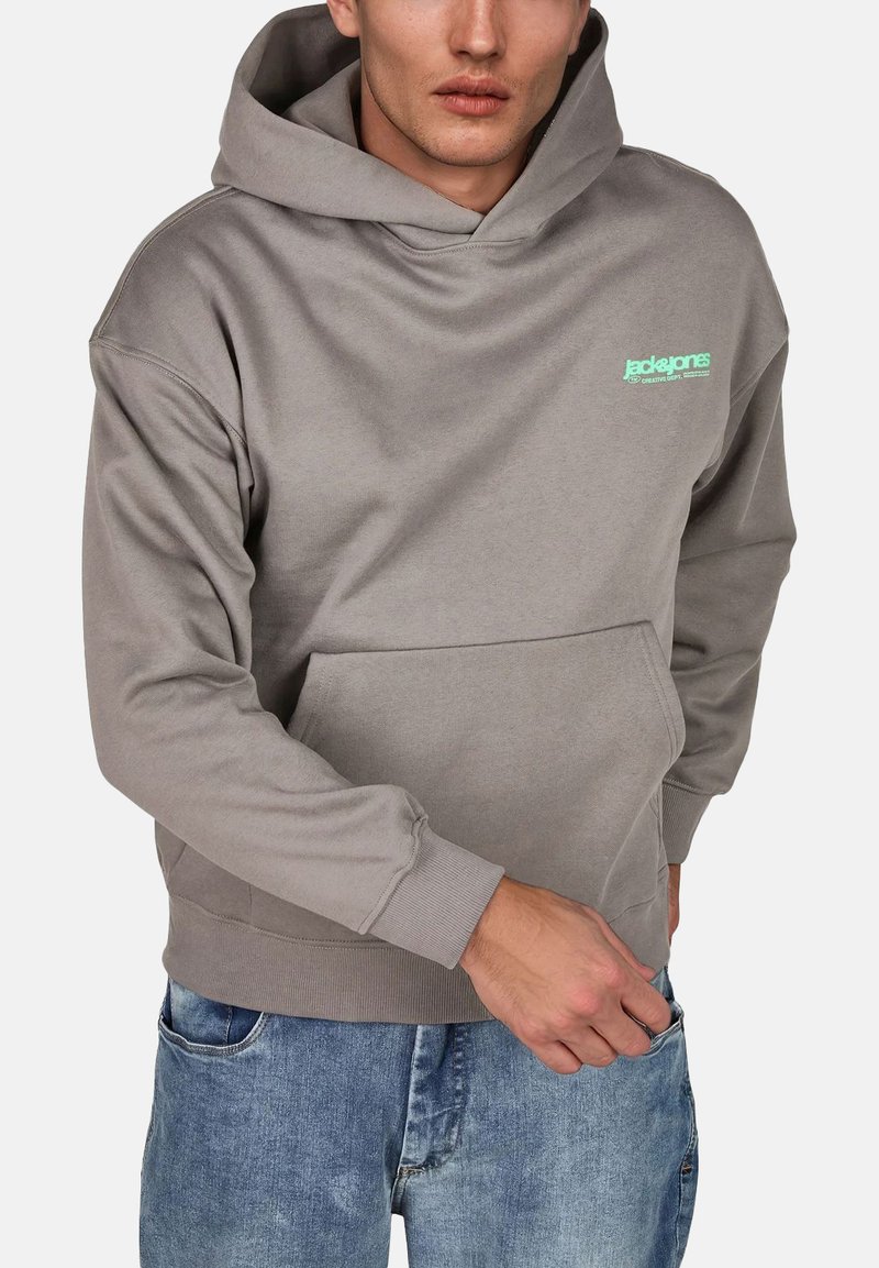 Sudadera gris hecha de una tela suave, con un bolsillo canguro y puños acanalados. Logo en verde menta en el pecho. Combinada con jeans de mezclilla azules.