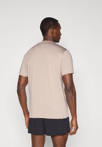 Μπεζ κοντομάνικη μπλούζα κατασκευασμένη από απαλό ύφασμα, με λαιμόκοψη crew και άνετη εφαρμογή, φορεμένη με μαύρο σόρτς.