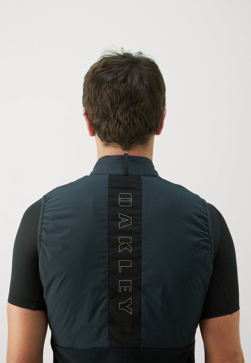 Schwarz und dunkelblaues Radtrikot mit einem Reißverschlusskragen, das auf dem Rücken ein auffälliges vertikales "OAKLEY"-Logo und strukturierte Ärmel aufweist.