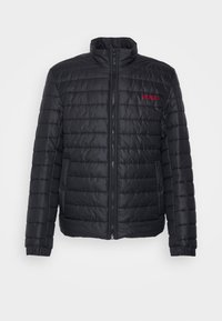Svart puffjacka med hög krage, horisontell kviltad design och elastiska muddar. Har en röd "HUGO" logo på bröstet.