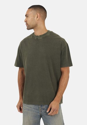T-shirt in cotone verde oliva con maniche corte, scollatura rotonda e vestibilità rilassata. Presenta una sottile texture lavata e dettagli cuciti.