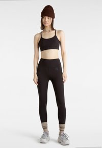 Schwarzer Sport-BH und hochgeschnittene Leggings aus dehnbarem Stoff. Das Outfit verfügt über flache Nähte und ein kleines Logo auf den Leggings.