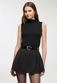 Top nero senza maniche abbinato a una mini gonna plissettata a righe nere, valorizzata da una cintura nera con fibbia argentata.