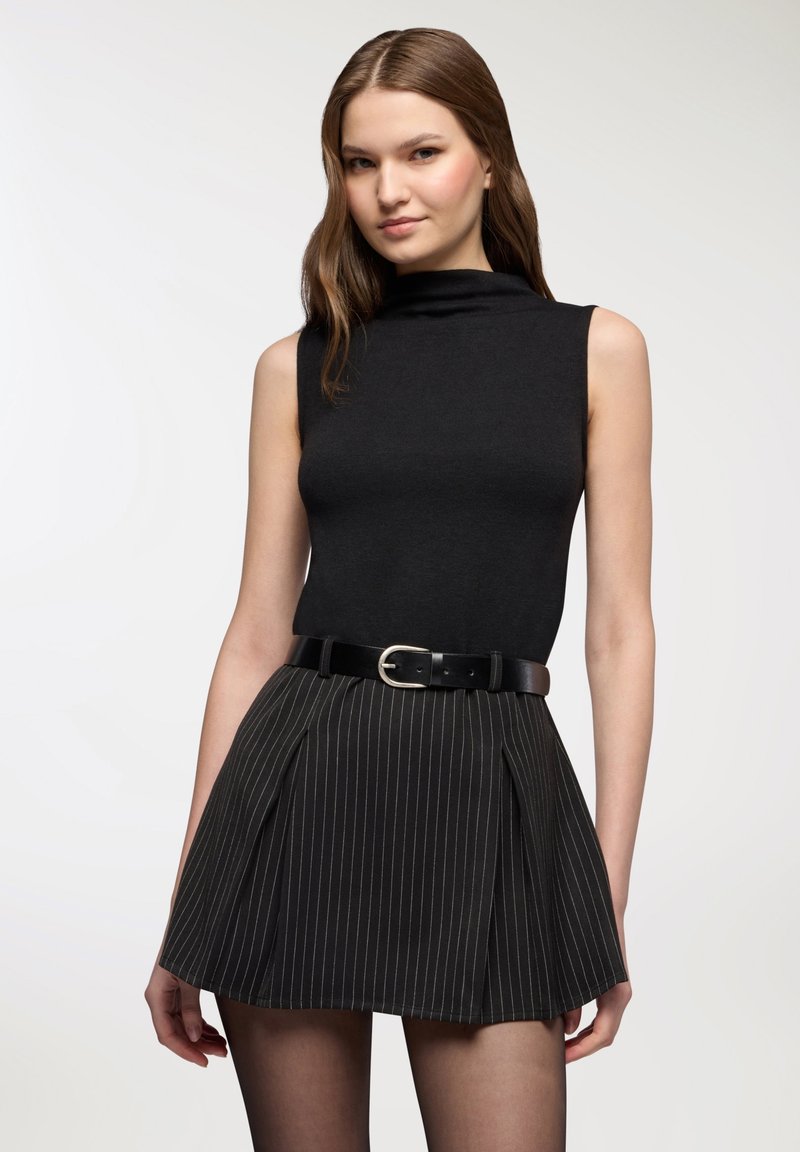 Top nero senza maniche abbinato a una mini gonna plissettata a righe nere, valorizzata da una cintura nera con fibbia argentata.